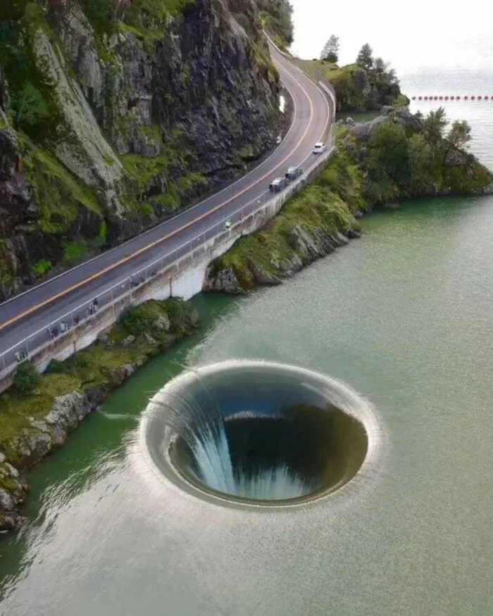 A giant spillway hole draining water near a mountain road, representing cool and interesting pics