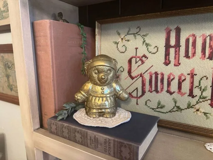 Vintage brass bear figurine thrift store find on bookshelf with cross stitch art