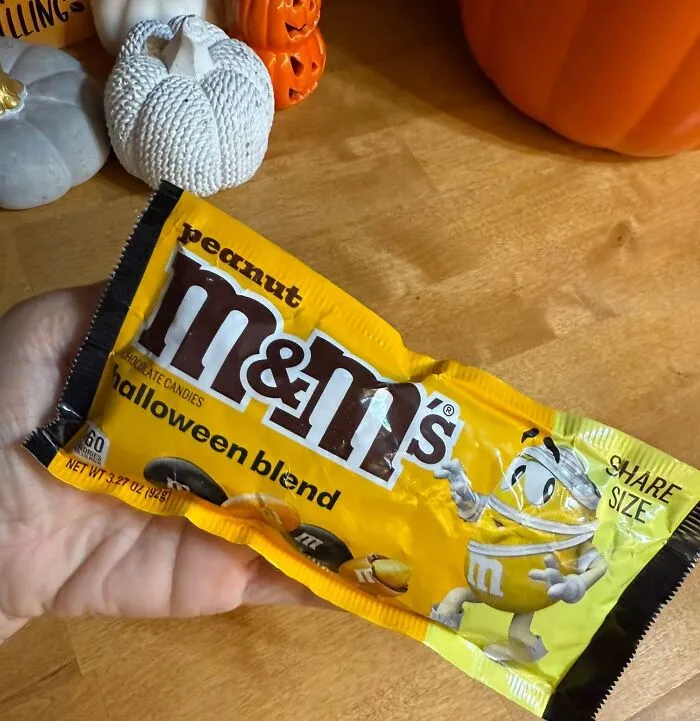 A hand holding a packet of Peanut M&M's Halloween blend, ideal as one of the best Halloween candies.