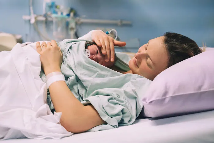 A happy mother holding her newborn baby in a hospital room, assisted by healthcare workers.
