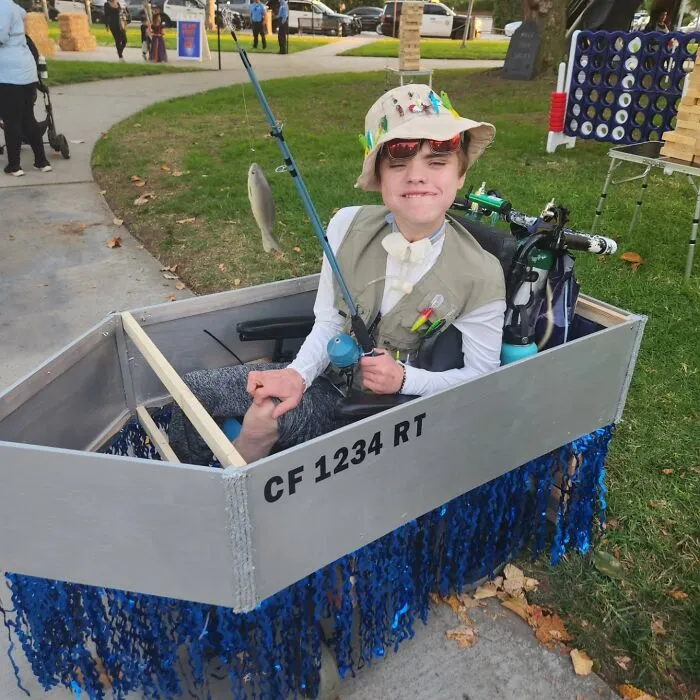 Boy in a fishing boat costume adapted for his wheelchair, showcasing creative Halloween ideas.