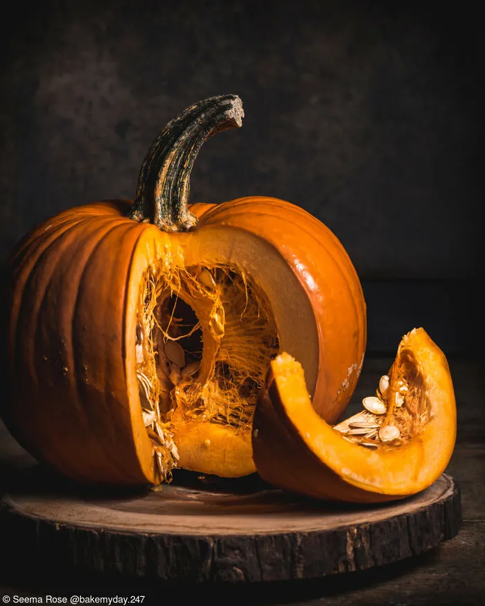 A sliced orange pumpkin with exposed seeds on a wooden board
