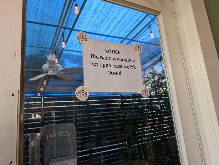 Absurd signs taped to a glass door reading that the patio is not open because it is closed.