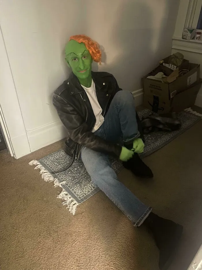 A person with green face paint and orange hair dressed as a goblin in a leather jacket for a Halloween costume idea.