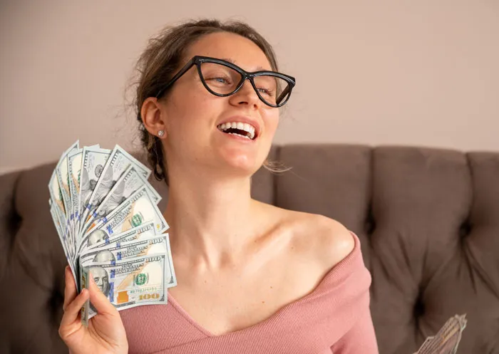 A smiling woman holding a fan of cash, representing financial gain mentioned in divorce stories.