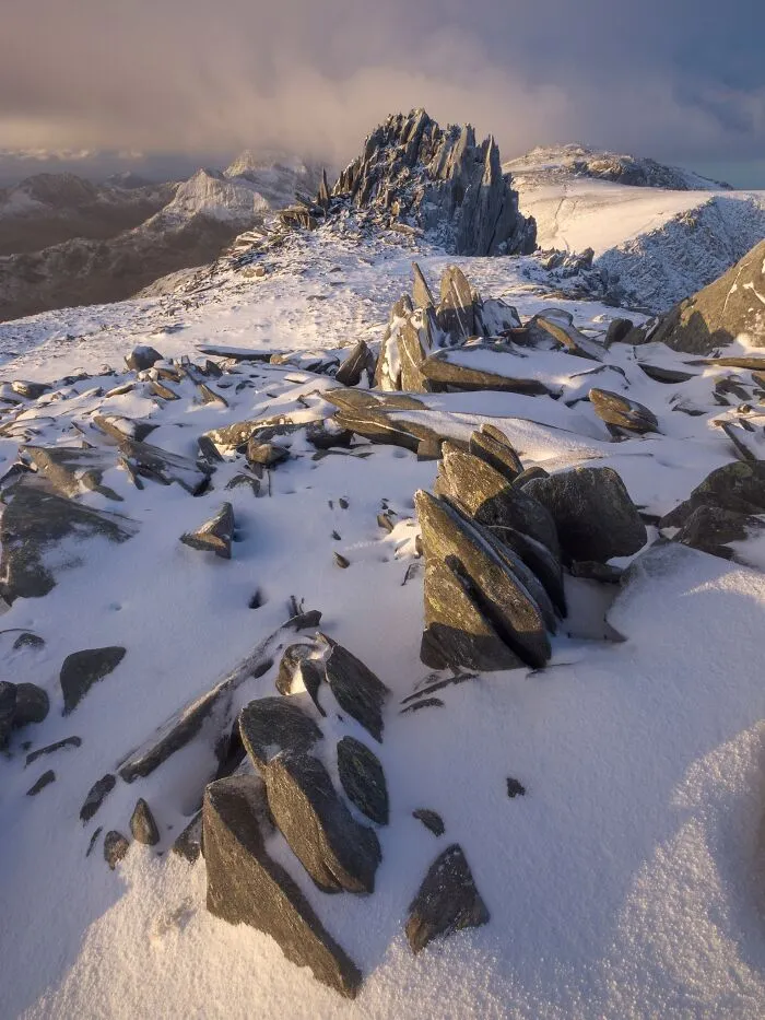Snow-dusted rocky mountain ridge bathed in warm light for Natural Landscape Photography Awards 2026.