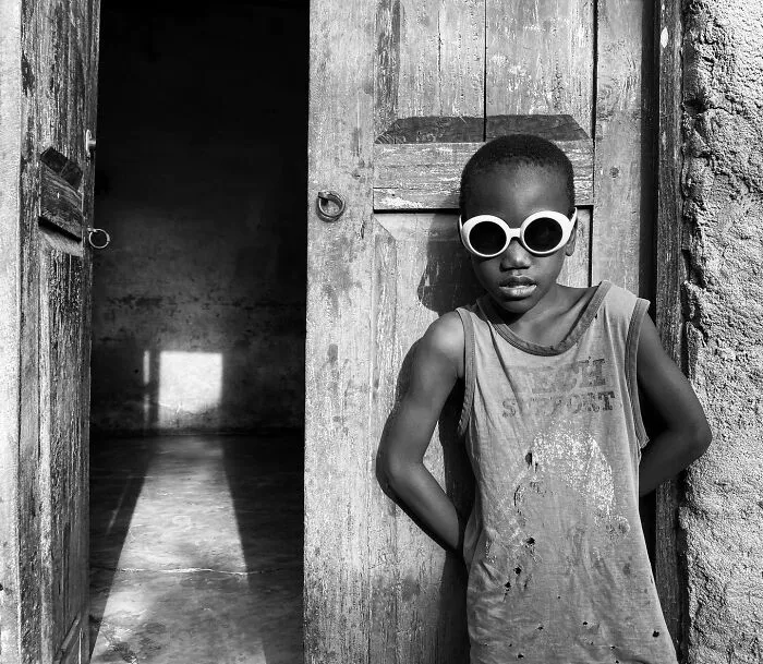 A black and white image of a young boy wearing sunglasses in a doorway, capturing human expression in portrait photos.