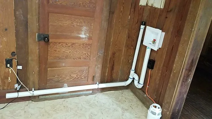Poorly installed plumbing and drain pipe running across a wooden door in a DIY home improvement attempt.