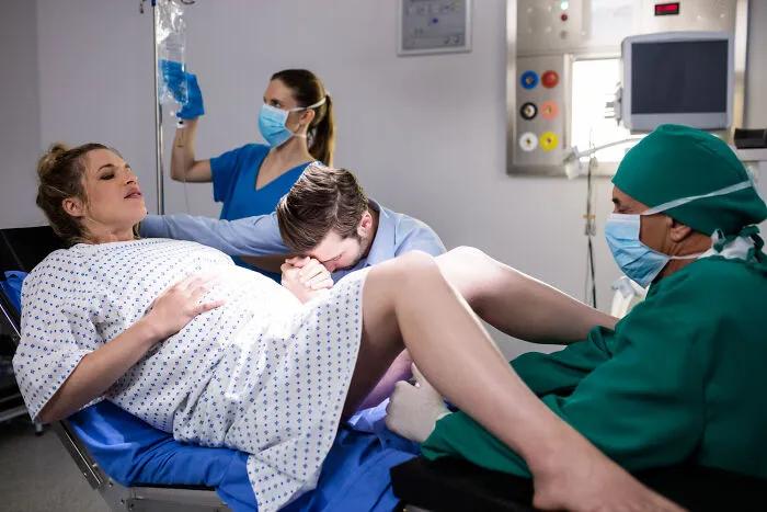 Healthcare workers assisting a pregnant woman during childbirth in a delivery room.
