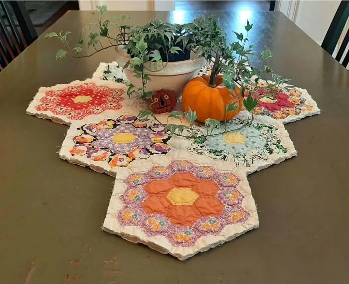 Colorful quilted hexagon table mat thrift store find with potted plants and pumpkin