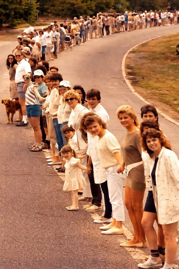 Long line of people holding hands outdoors, evoking nostalgic photos of '80s kids childhoods.