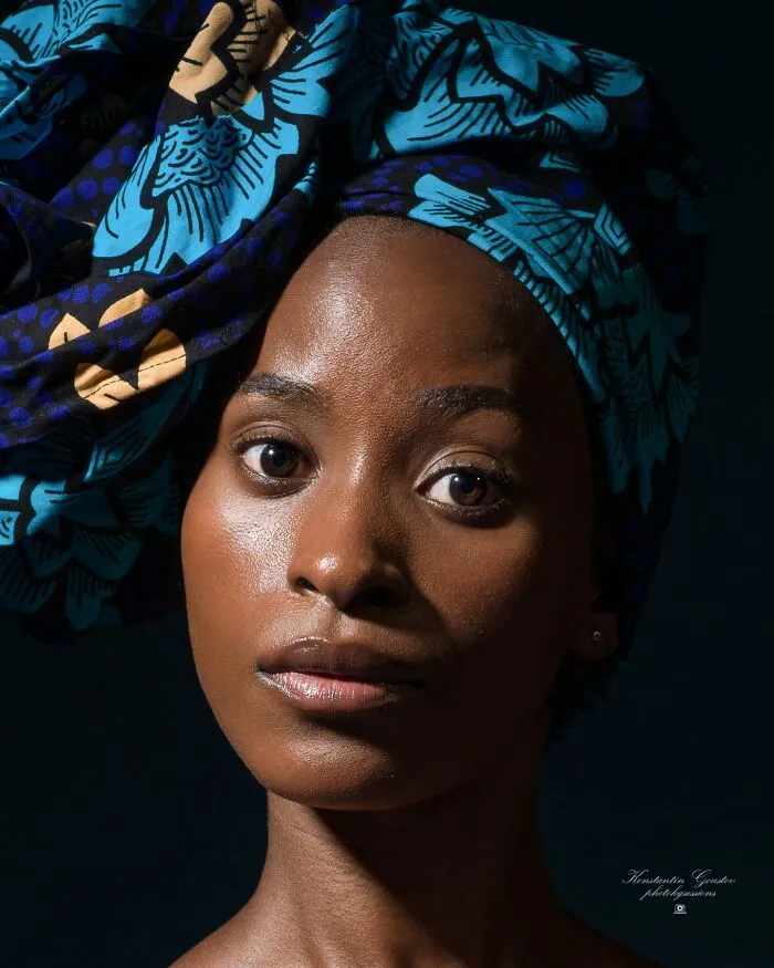 A striking portrait photo of a woman wearing a blue patterned headwrap, showcasing intense human expression.