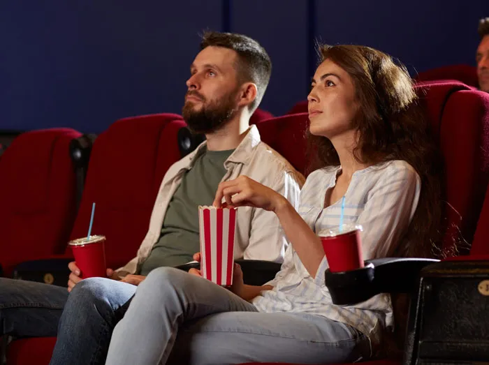 A couple sitting in a movie theater with popcorn, experiencing an awkward moment before deciding to skip a second date.