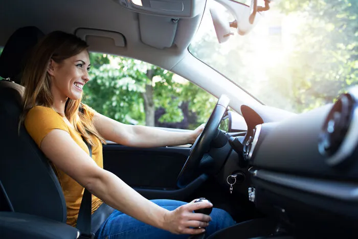 A smiling woman driving a car safely, demonstrating essential vehicle emergency tips.