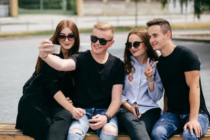 Group of friends taking selfie sitting on bench outdoors with sunglasses