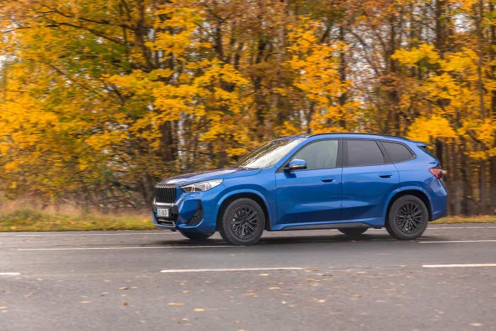 Blue SUV driving on road with autumn trees background