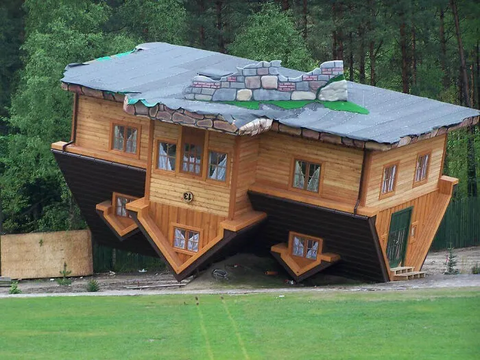 An upside-down house with a bizarre shape sits on its roof in a grassy field.