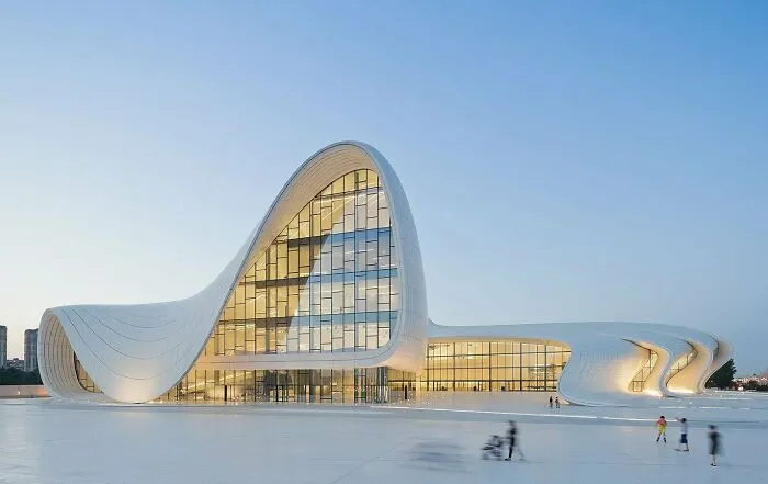 A white futuristic building with bizarre shapes of flowing curves and walls made of glass under a clear sky.