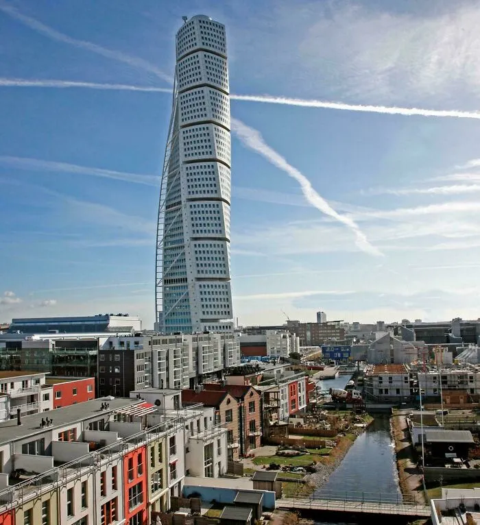 A twisting white skyscraper, showing off bizarre shapes that challenge ordinary architecture, in a coastal city.