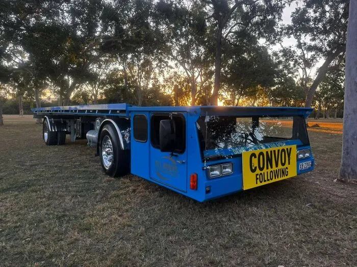 Extremely low-profile blue flatbed truck with a yellow sign, showcasing weird and wonderful vehicles.