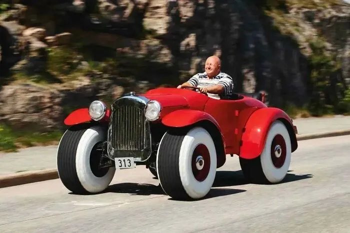 A man driving a custom cartoonish red roadster with huge whitewall tires, one of the wonderful vehicles.
