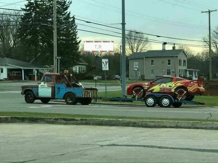 Life-size Tow Mater tow truck pulling a Lightning McQueen race car trailer, showcase of weird and wonderful vehicles.