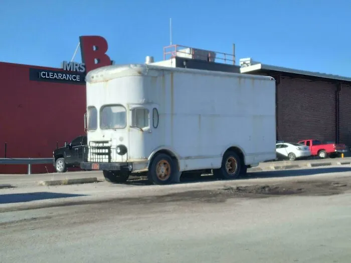 An unusually tall white vintage box truck parked outdoors, showing unique custom vehicle modifications.