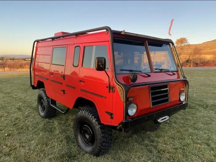 Red vintage Volvo off-road military truck parked outdoors on a grassy lawn.