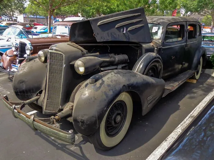 A black vintage car with an open hood, showcasing wonderful vehicles at an outdoor show.