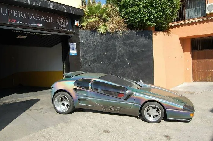 Iridescent sleek sports car parked outside a garage, showcasing a unique design.