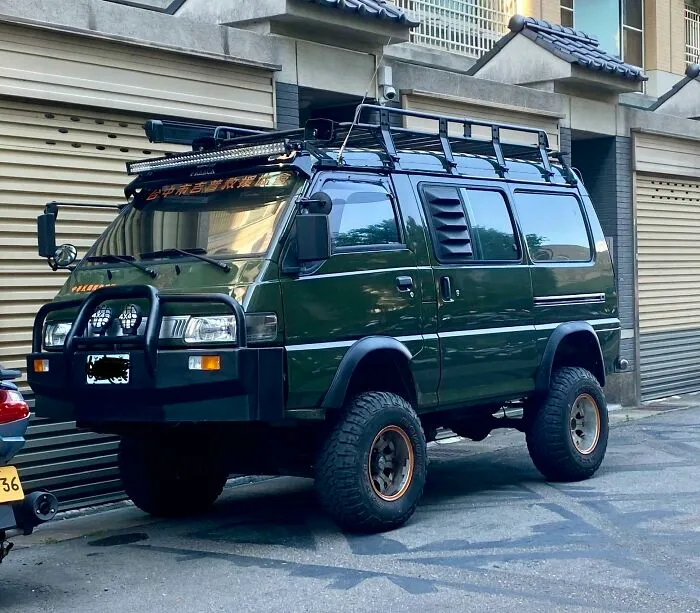 Lifted dark green off-road van with heavy-duty bumper and roof rack, featuring weird and wonderful vehicles.