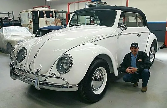 Man posing next to an oversized white VW Beetle custom vehicle.