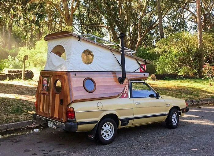 Small pickup truck transformed into a custom camper van with wood paneling and pop-up tent, among weird vehicles.