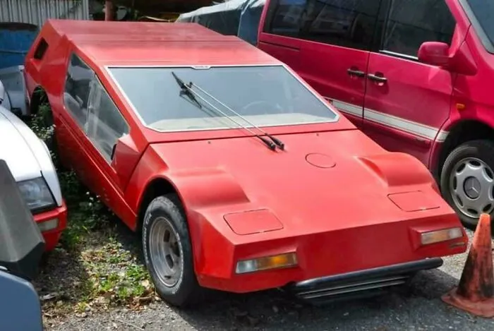 Futuristic red wedge-shaped car parked outdoors, representing weird and wonderful vehicles.