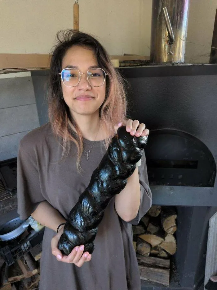 A woman smiling and holding burnt challah bread, showing how things went wrong.