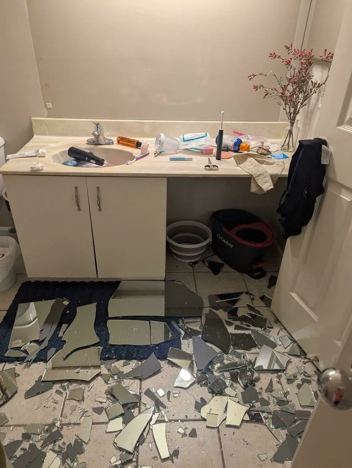 A shattered bathroom mirror on the floor tiles, representing things went wrong pics in home improvement.