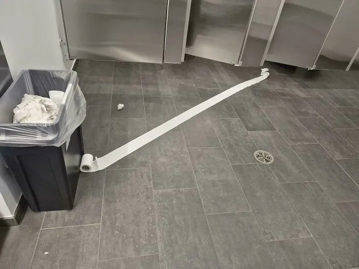 A long trail of toilet paper on a public restroom floor showing things went wrong.