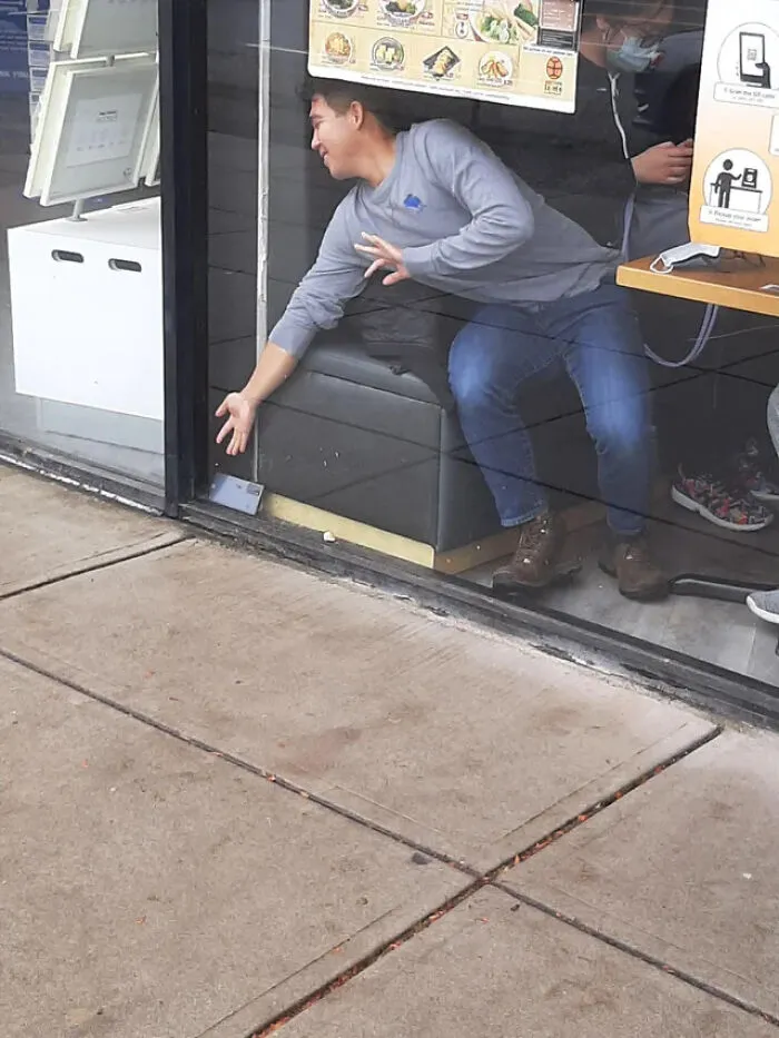 A man tries to reach his dropped phone through a glass window in Things-Went-Wrong-Pics