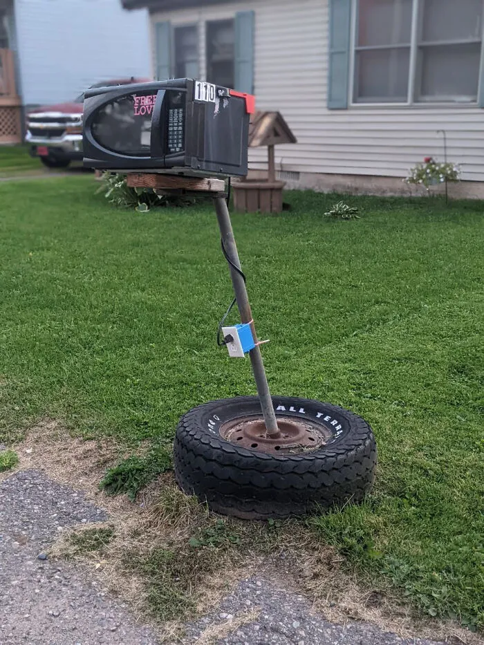 A creative DIY project showing a mailbox made from an old microwave on a post inside a tire.
