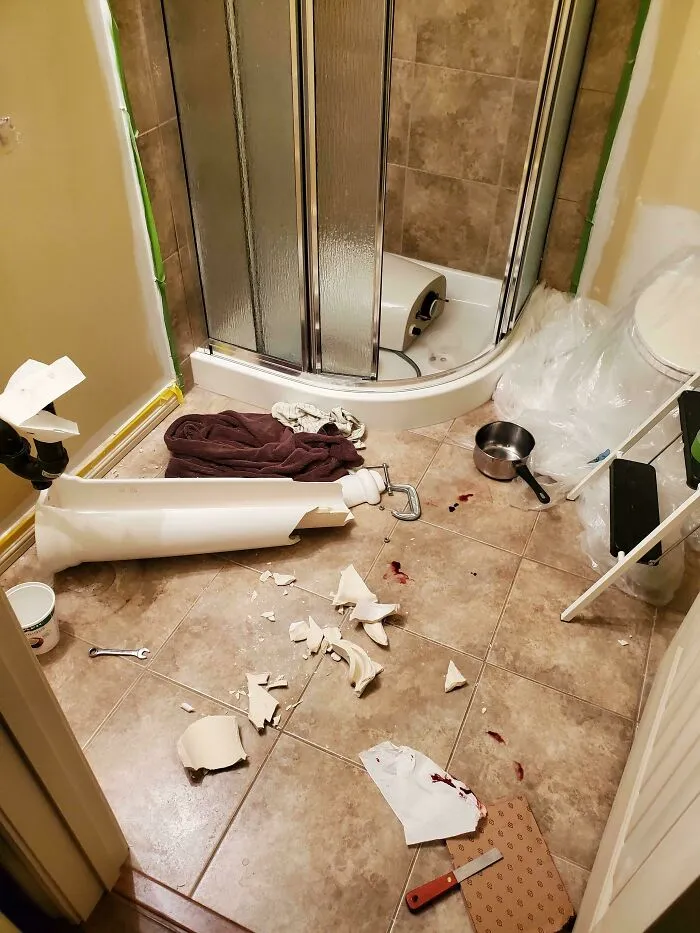A messy bathroom floor covered in broken ceramic pieces from a failed bathroom renovation DIY project.