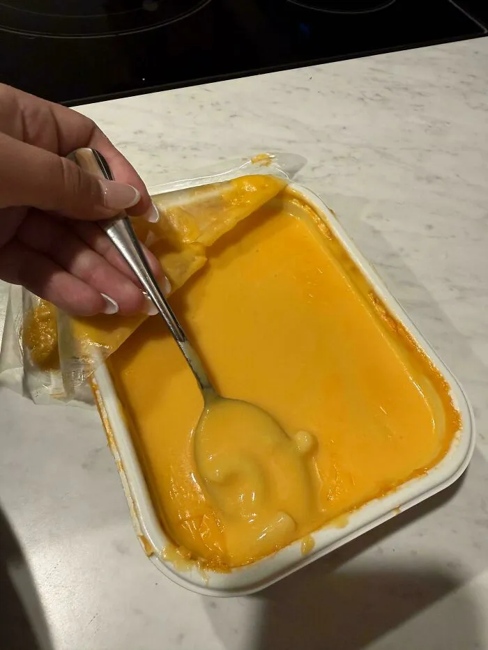 A spoon dipping into a container of orange sauce where the plastic film didn't peel off correctly.