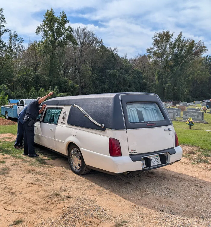 A white hearse parked on a dirt road, where things went wrong with transport.