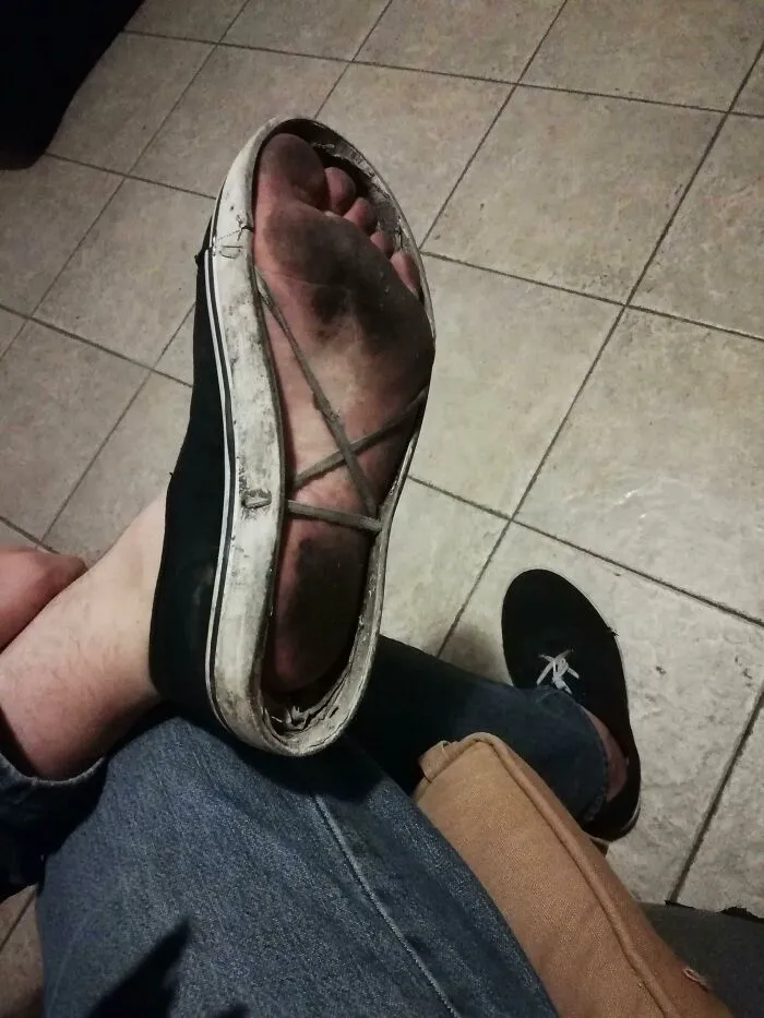 A black canvas shoe with the entire sole missing, exposing a dirty bare foot from DIY projects.