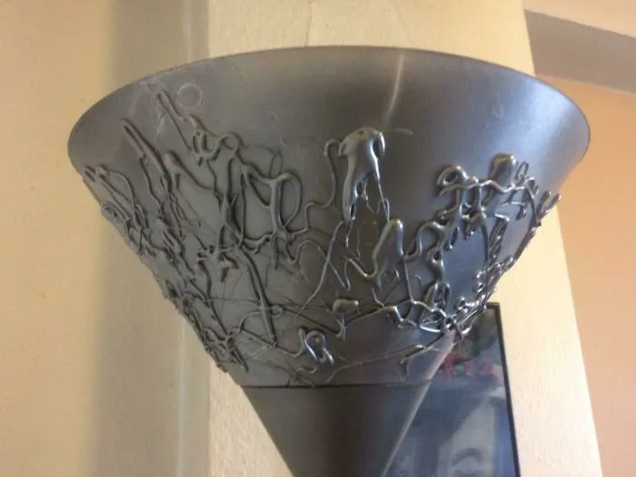 A custom DIY lamp shade decorated with abstract patterns using a hot glue gun and metallic spray paint.