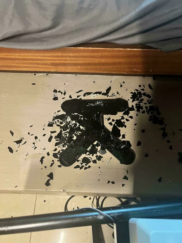 Shattered glass pieces on a wooden floor under a desk showing things went wrong.