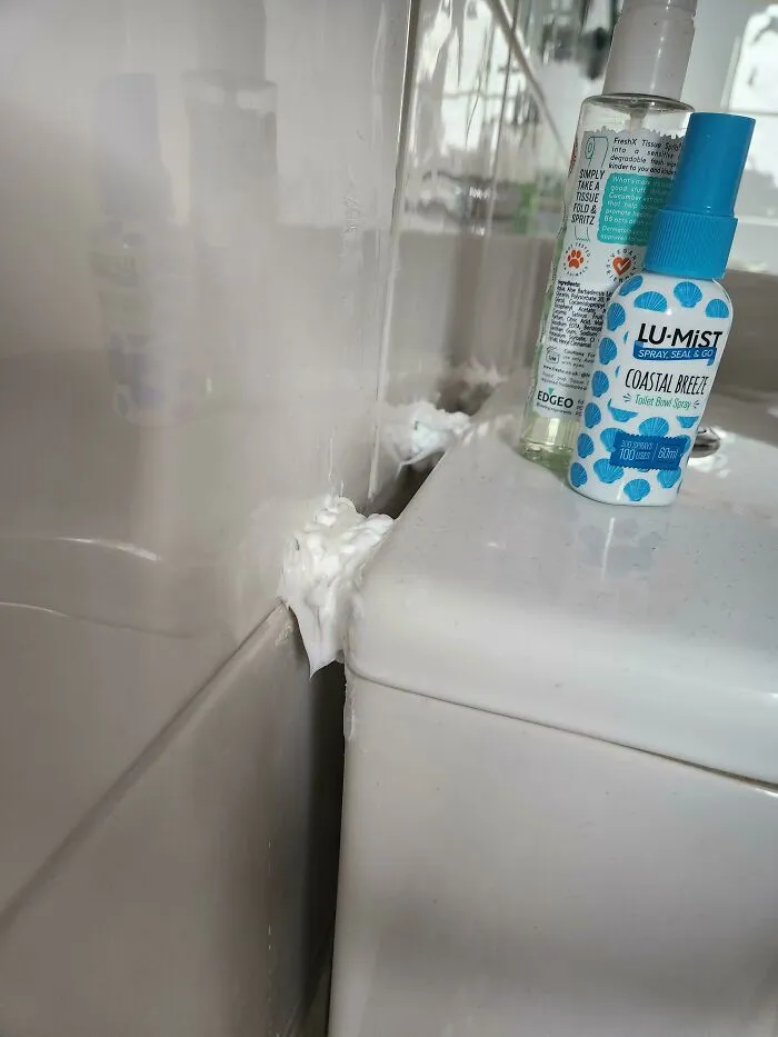 Excessive white sealant foam applied between a bathroom sink and wall as a failed DIY project.