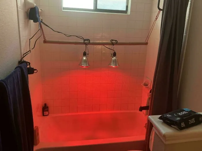 A questionable DIY project featuring two red heat lamps suspended above a white bathtub with a rod