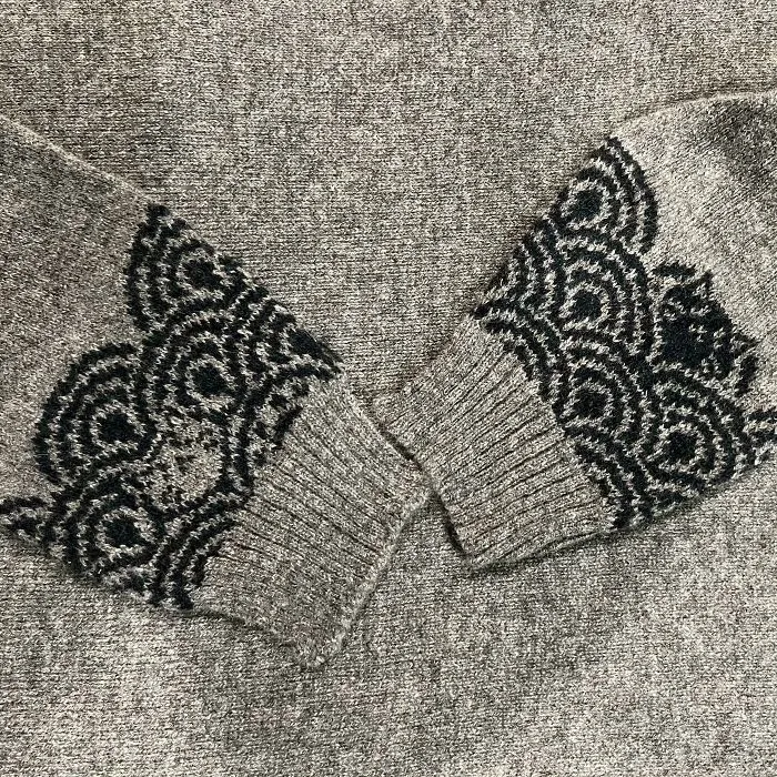 Detailed close-up of a hand-knitted grey sweater sleeves featuring intricate black patterns, highlighting amateur knitting.