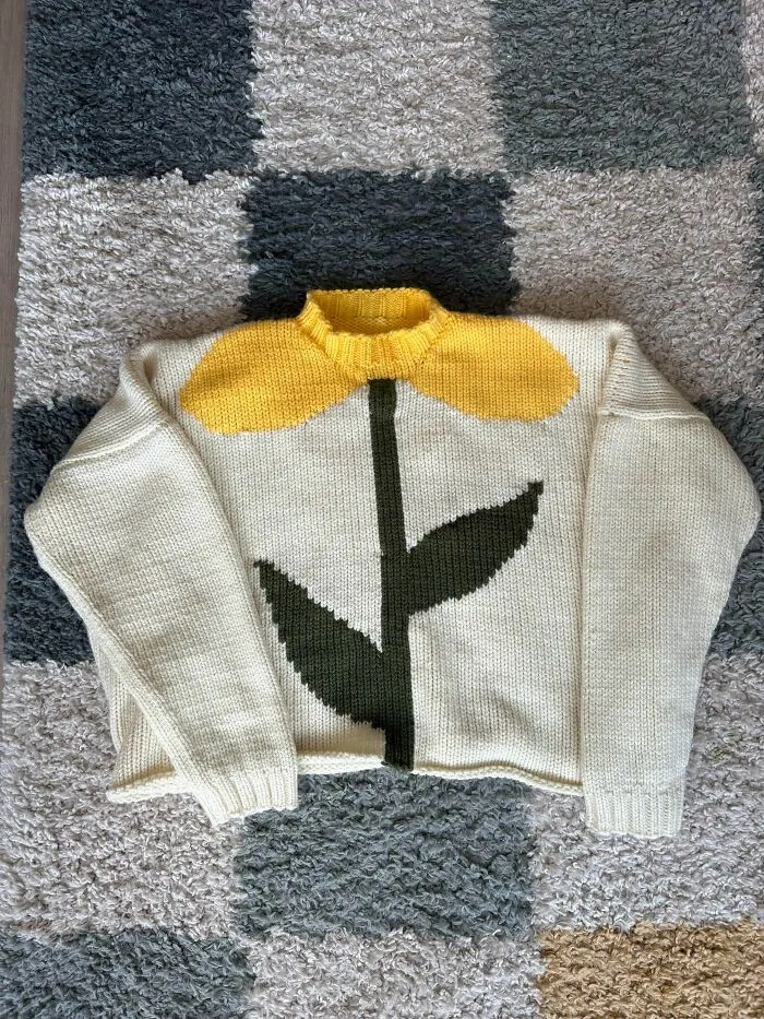 A cozy off-white knitted sweater with a large yellow flower design, showcasing creative knitting.