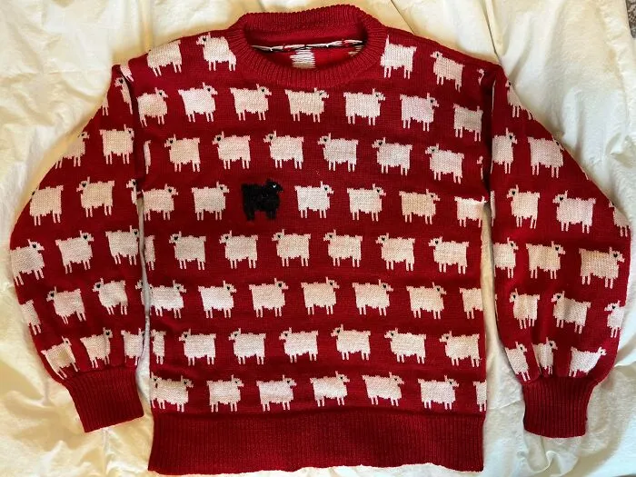 A classic red sweater featuring rows of white sheep and one black sheep, showcasing detailed knitting.